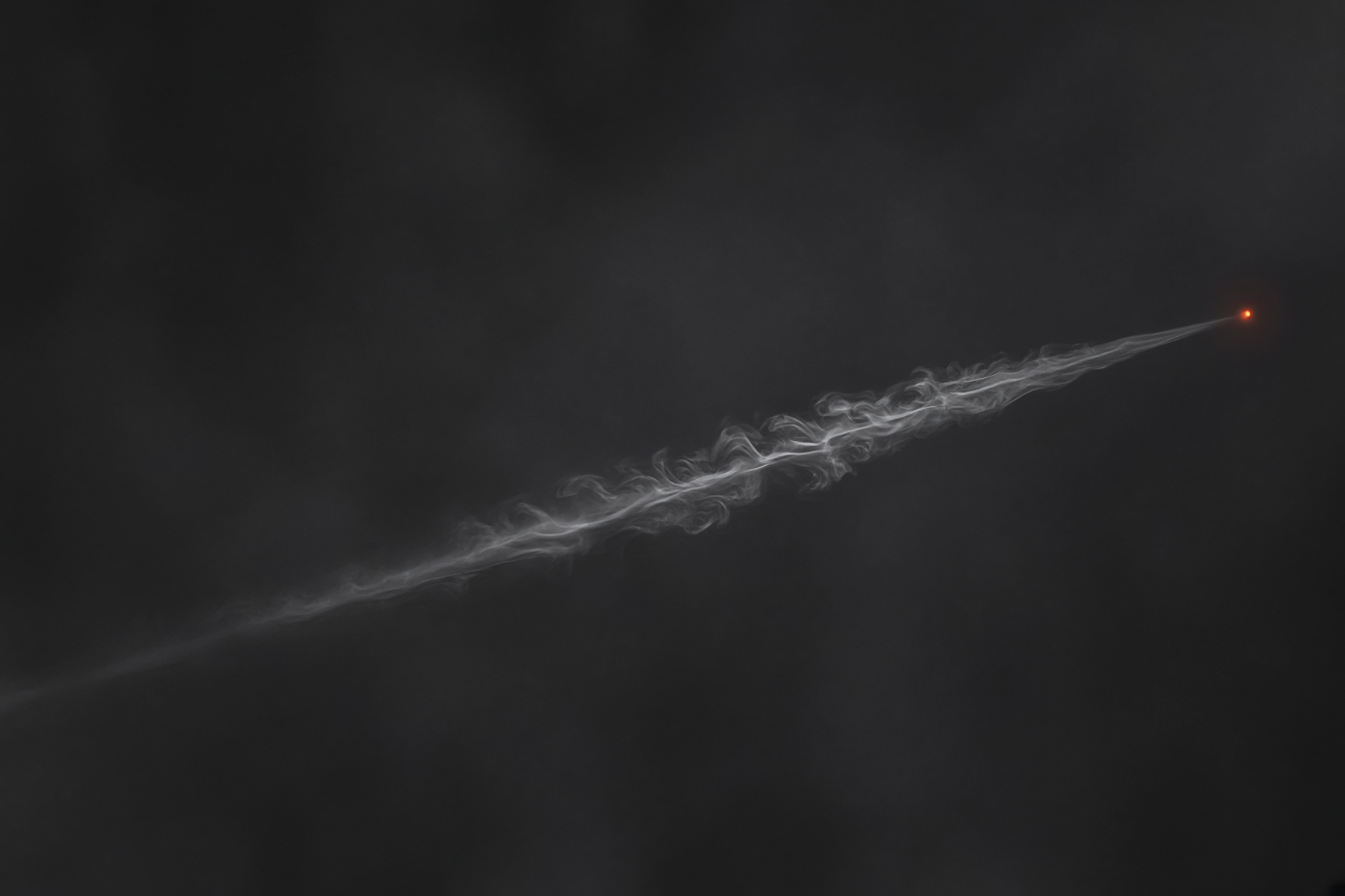A thin smoke trail with a small orange point against a dark sky